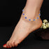 A foot with red nail polish wearing a 14k gold-filled anklet featuring blue Evil Eye charms from the Blue Evil Eye Charm Bracelet for Protection Good Luck Turkish Nazar rests against a dark background, with white roses peeking from the corner.